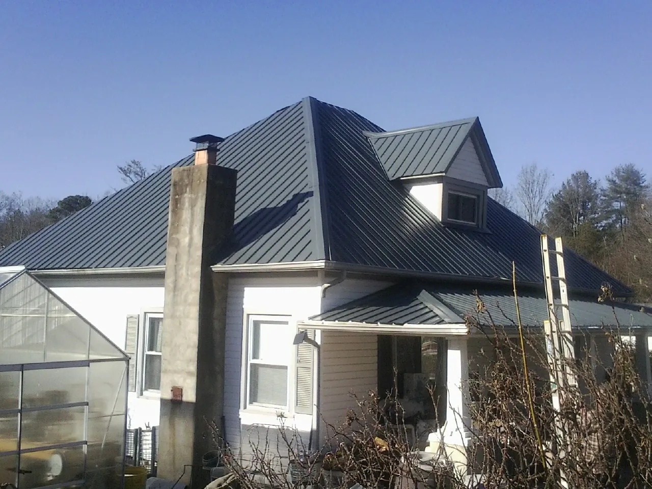 Dark blue standing seam metal roof on a white farmhouse with dormer — Slate & Tile Roof Repair by Roofing Brothers in Coyle