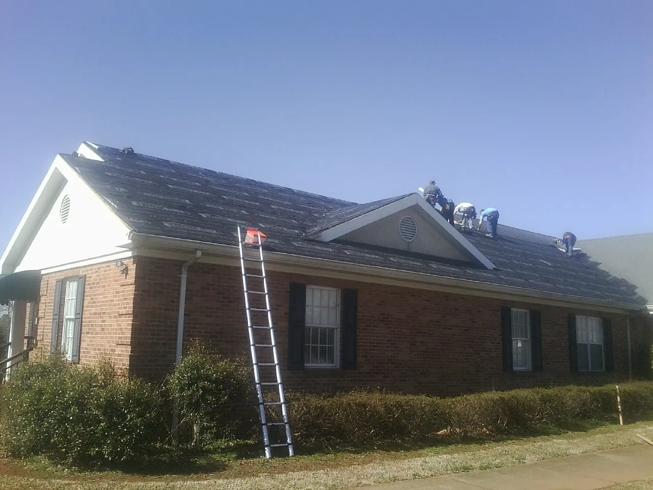Crew tearing shingles off a brick ranch roof with a ladder set — Metal Roof Repair work by our crew in Coyle