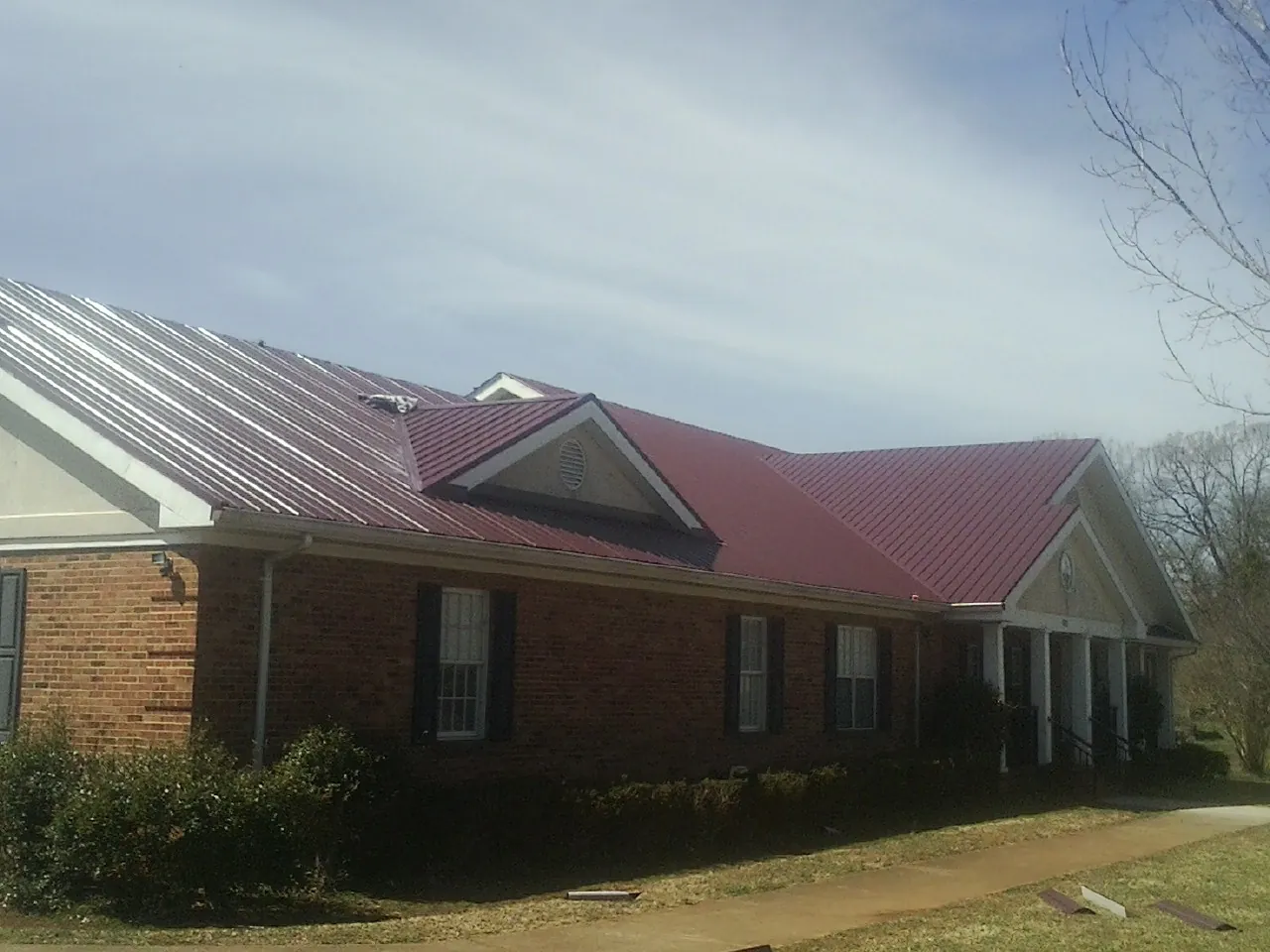 Red metal roof with gabled entries on a long brick building, from a Hail Damage Roof Repair job in Coyle