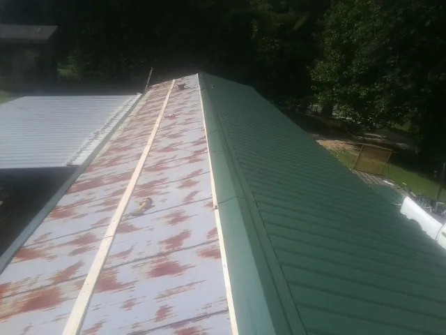 Old rusted panels beside newly installed green metal roofing — Wind Damage Roof Repair by Roofing Brothers in Coyle