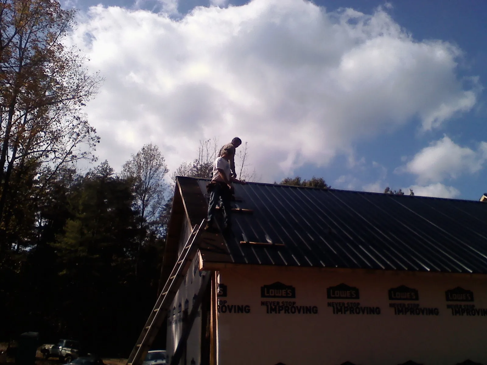 Roofer fastening dark metal panels high against a cloudy sky, from a Roof Inspection job in Coyle