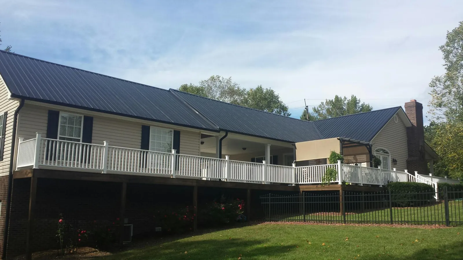 Black metal roof above a long white railed deck on a hillside home in Coyle