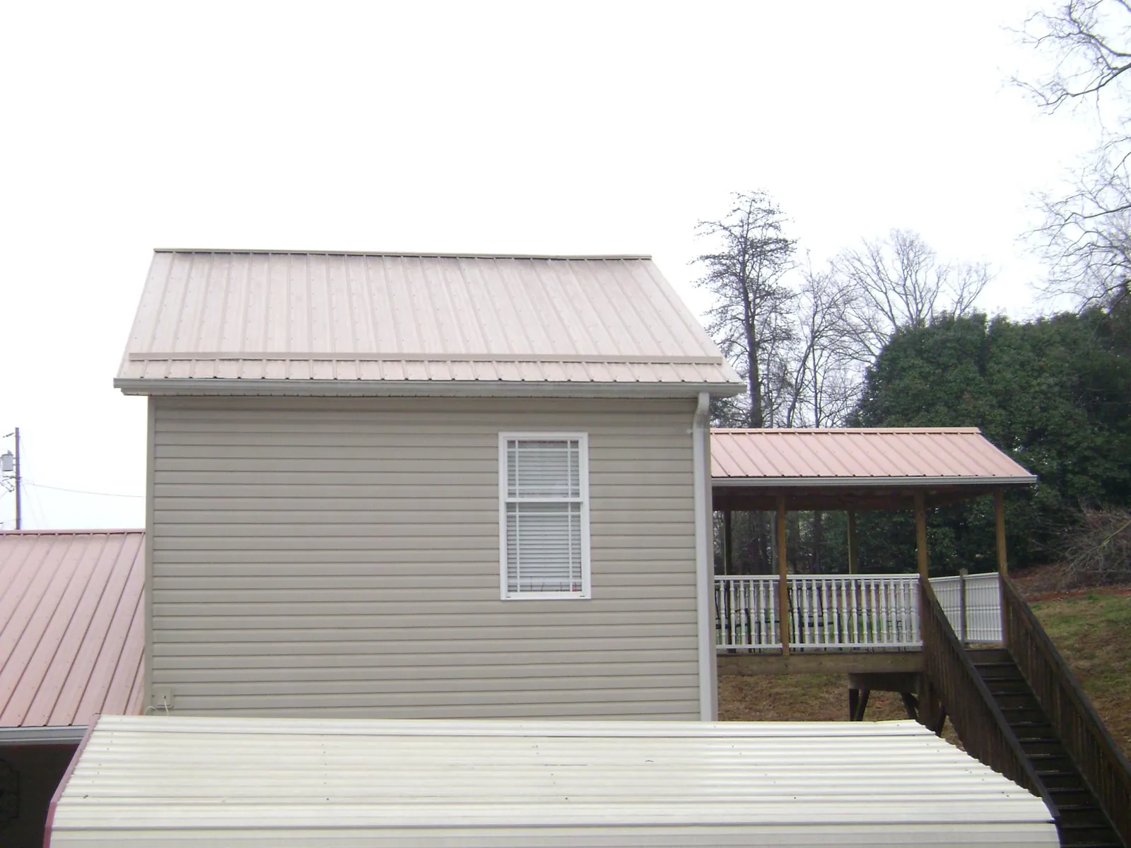 Tan metal roofs on a two story addition and attached porch, from a Roof Replacement job in Coyle